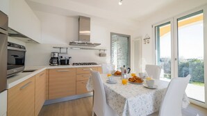 A modern kitchen with a dining area, featuring a stainless steel stove, a coffee maker, and a table set with plates, cups, and a pitcher of orange juice. - il giardino di Laura (Pompeiana)