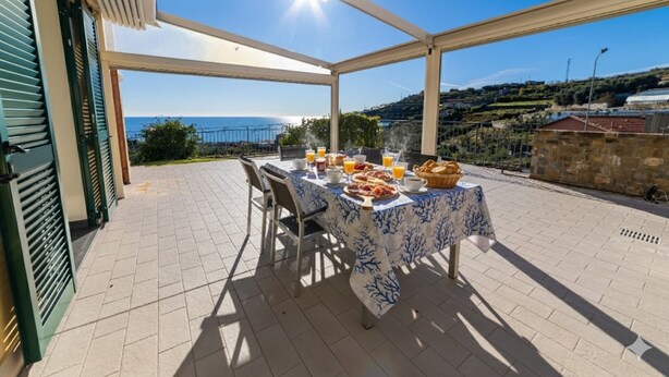An outdoor dining area with a table set for breakfast, overlooking a scenic view of the sea and hills. - il giardino di Laura (Pompeiana)