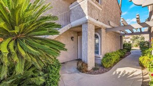 A building with a stone facade, a balcony, and a pathway leading to the entrance. - Sunny Desert Escape - A Ryson Property (Palm Springs)