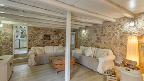 Una habitación rústica con paredes de piedra, un sofá blanco, un cofre de madera y una chimenea.