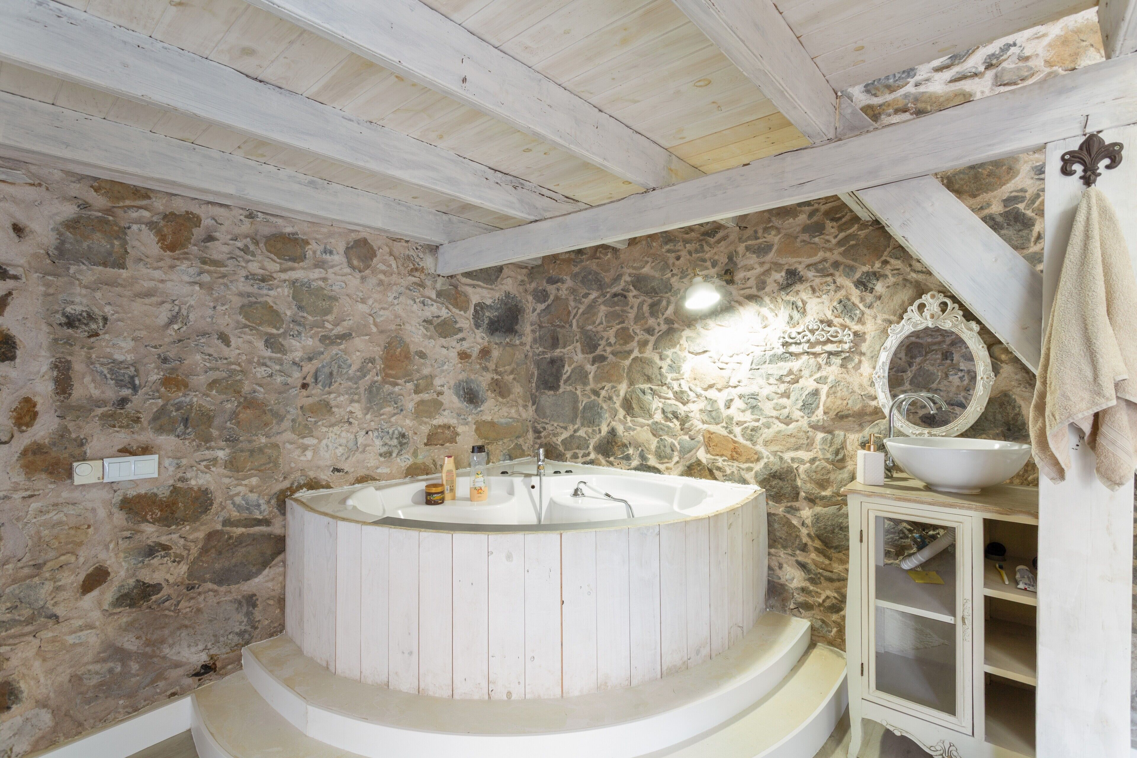 Ein Badezimmer mit Steinwänden, einer runden Badewanne, einem Holzkosmetikschrank und einem Spiegel.