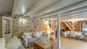 Un interior rústico con pared de piedra, vigas de madera, un sofá, una mesa y una escalera.
