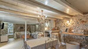 Un interior rústico con pared de piedra, una araña, una mesa de comedor y una chimenea.