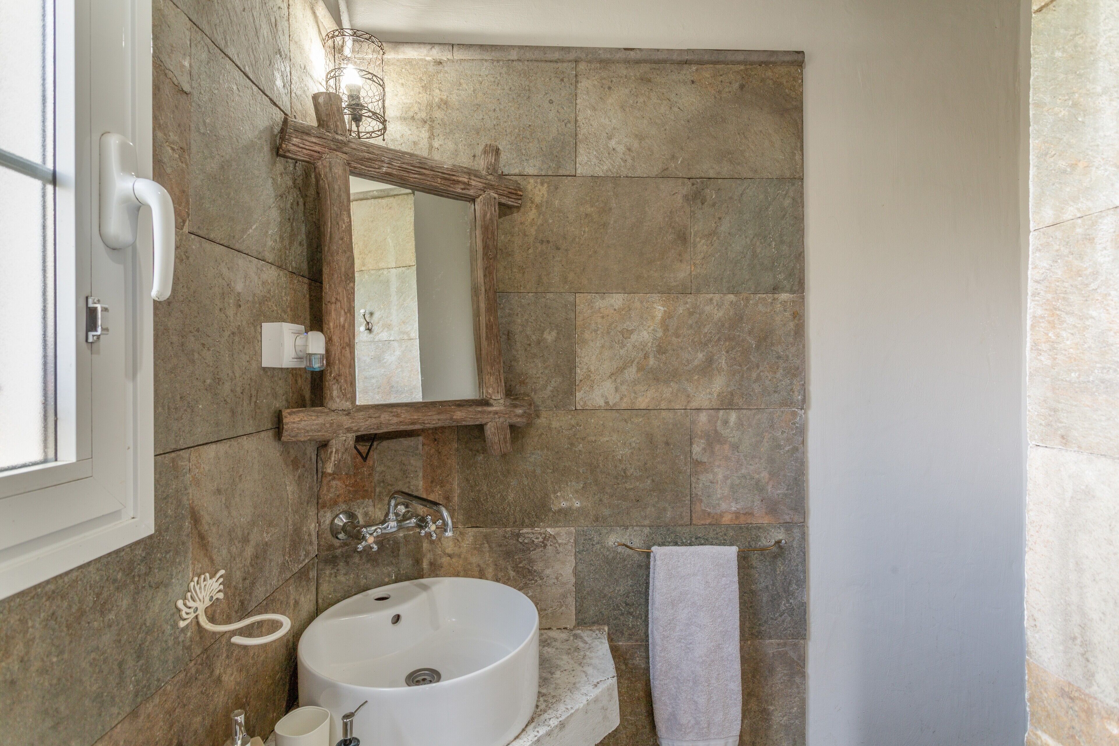 A bathroom with a stone wall, a wooden-framed mirror, a white sink, and a towel rack.
