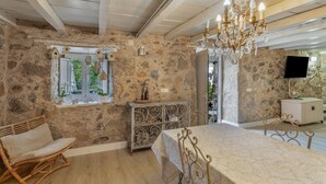 Una habitación de paredes de piedra con una mesa de comedor, candelabro, silla de mimbre y un televisor.