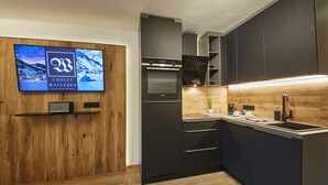 Une cuisine moderne avec des meubles de couleur sombre, un four encastré et un mur d’accent en bois.