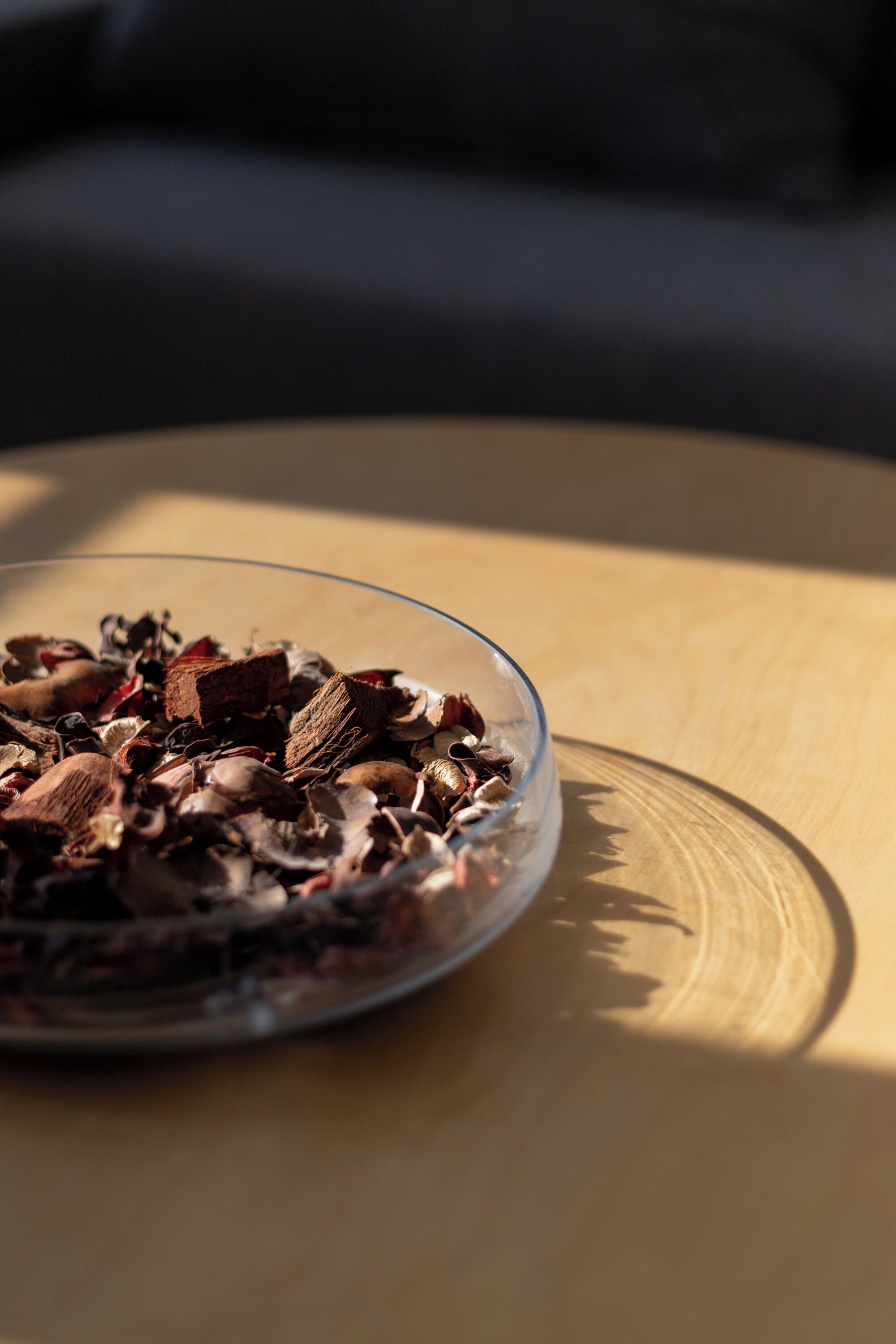Un saladier en verre transparent, rempli d’un assortiment de fruits secs et de noix, est posé sur une surface en bois.