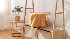 Una poltrona a dondolo in legno con seduta e schienale intrecciati, un tavolino tondo con una pianta e uno specchio appeso al muro.