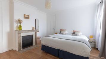 A bedroom with a bed, a fireplace, a nightstand, and a mirror on the wall.