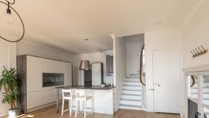Una cucina moderna con mobili bianchi, un'isola centrale con posti a sedere, una scala e una pianta in vaso.