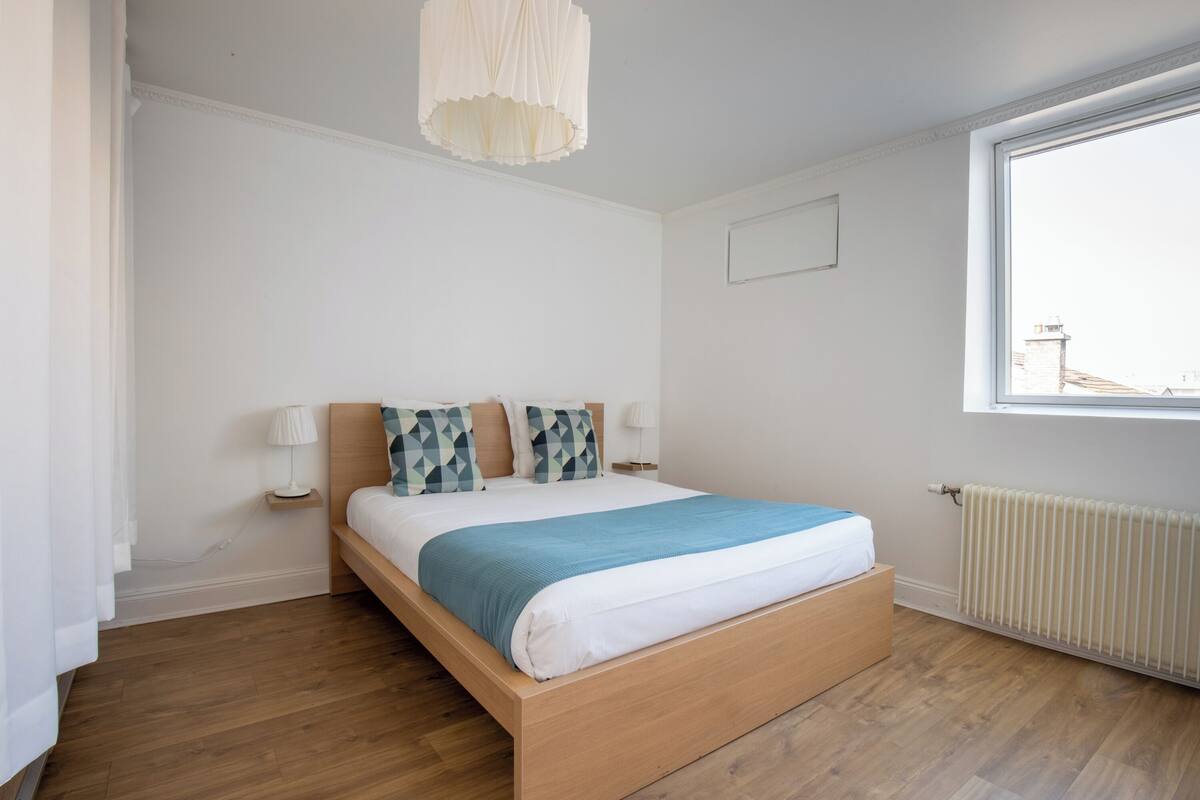 A bedroom with a wooden bed, white walls, a window, and a radiator.