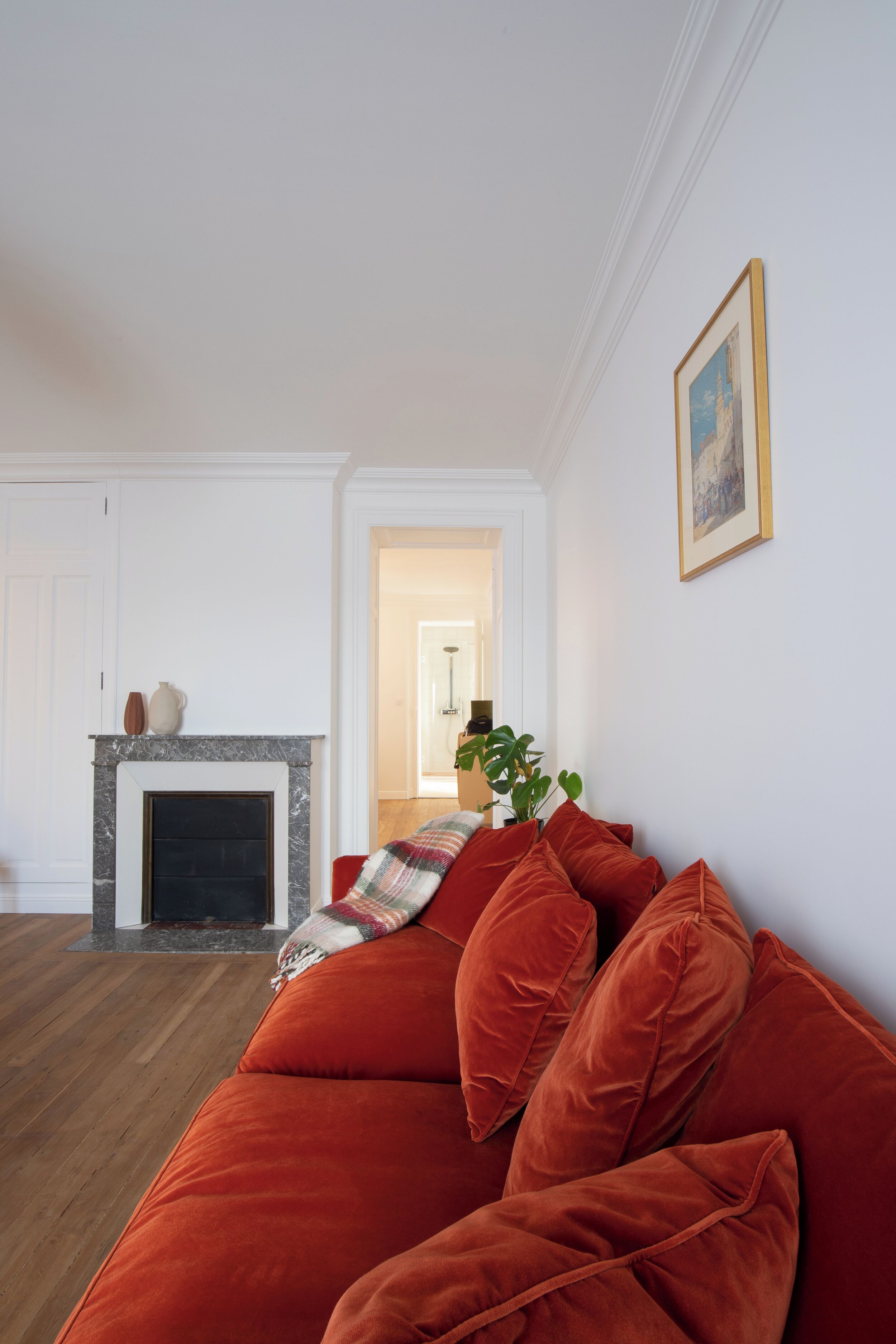 Un salon avec une cheminée, un canapé rouge et un tableau encadré au mur.