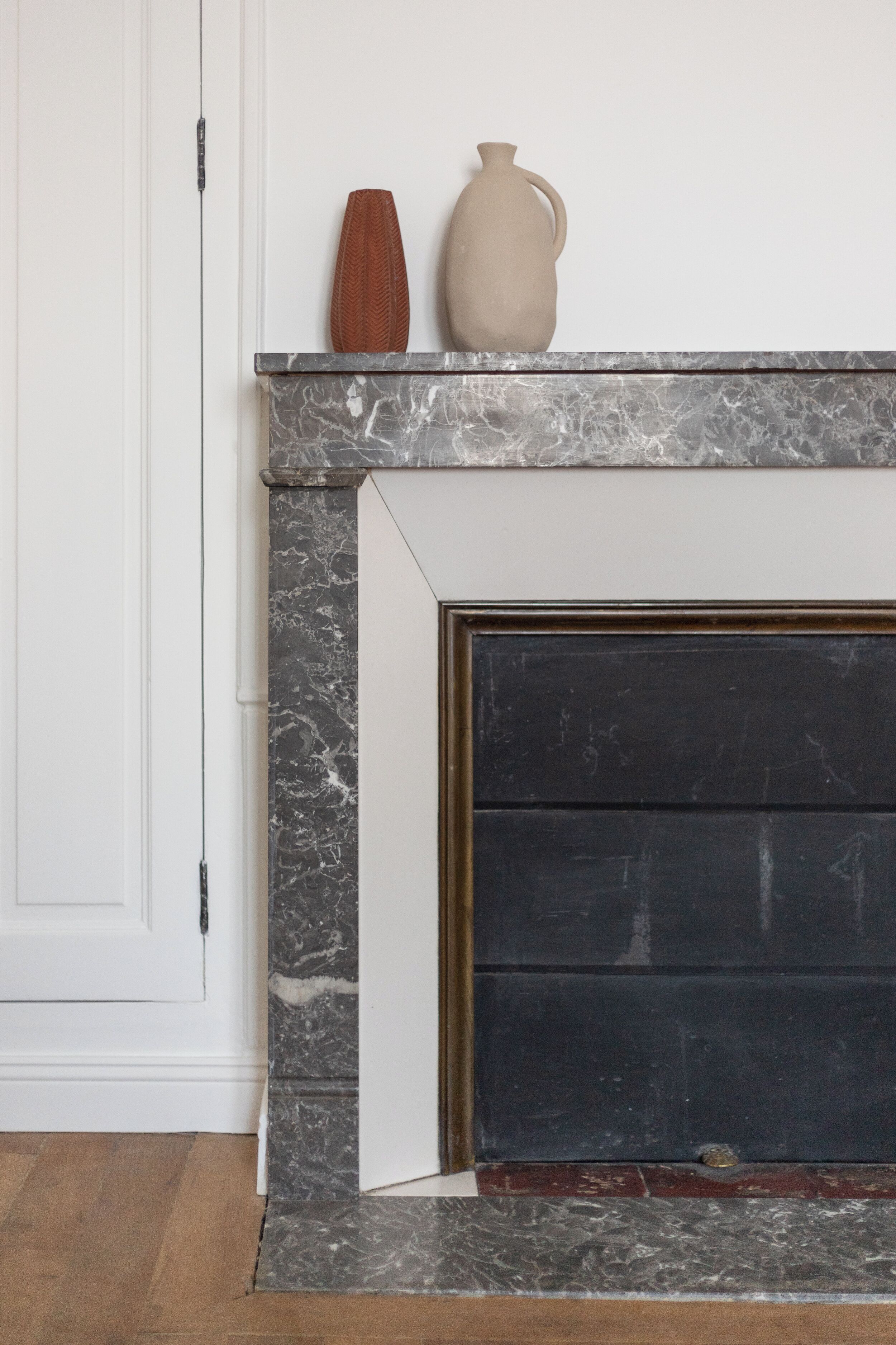 A fireplace with a marble surround, a white door, and a wooden floor.