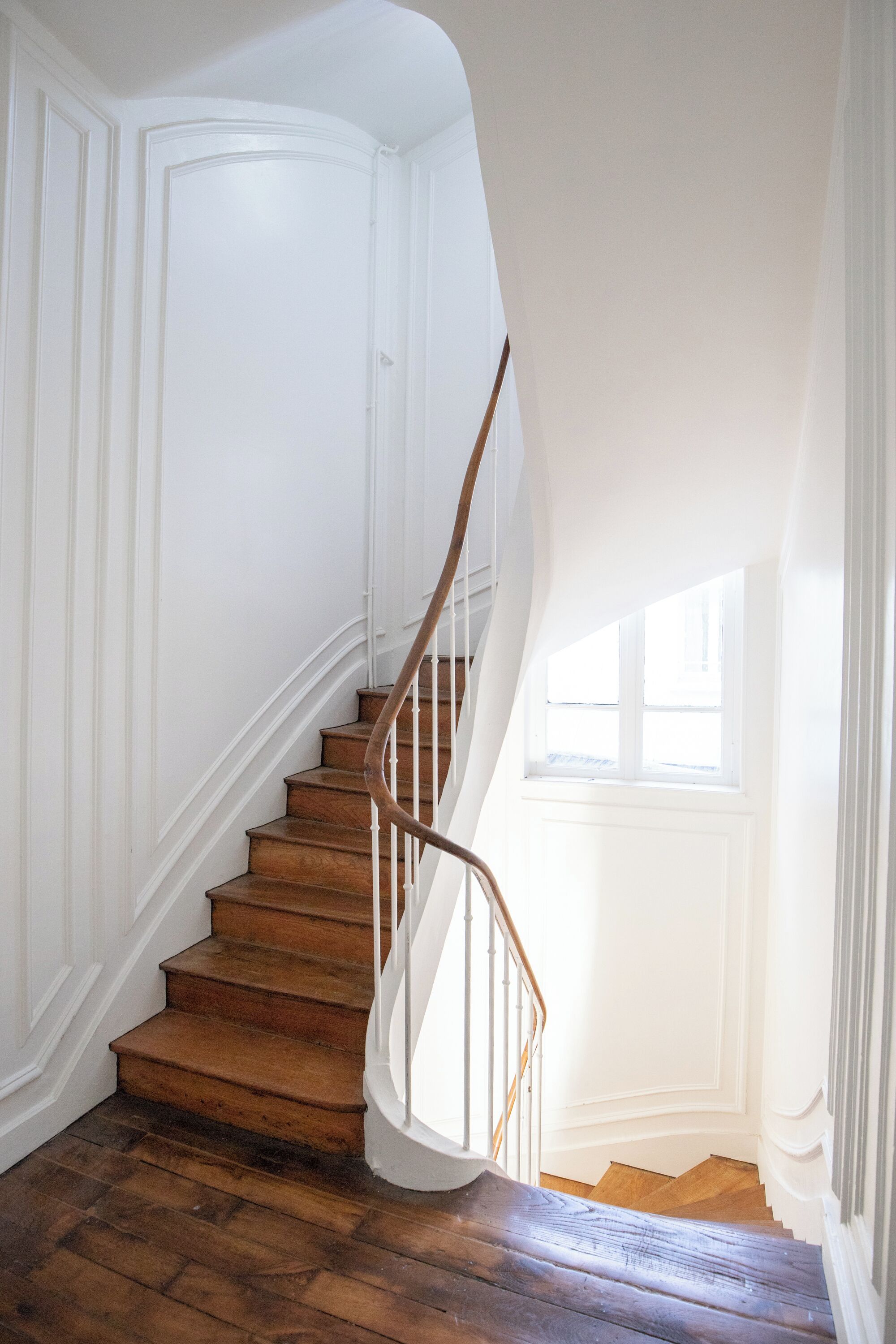Eine Holztreppe mit weißen Wänden und einem Fenster am oberen Ende.
