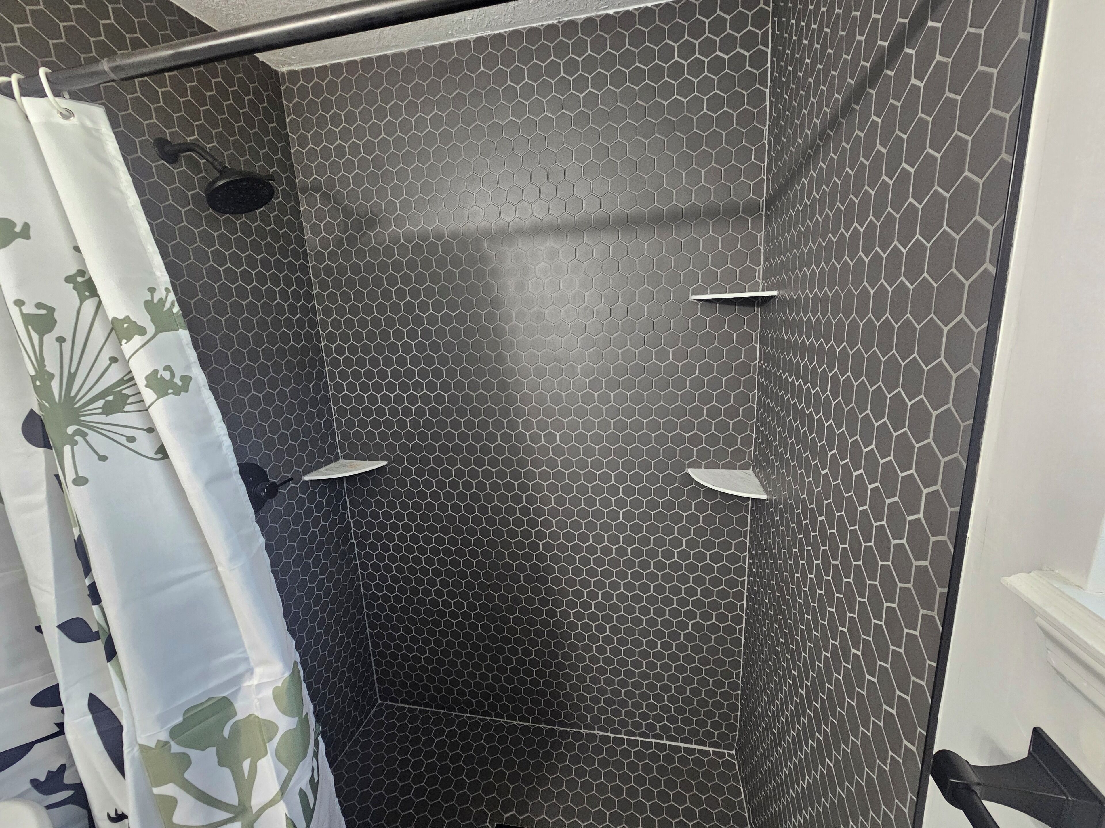 A shower area with a hexagonal tile pattern, a shower curtain with a floral design, and a handheld showerhead.