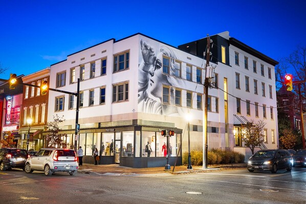A building with a large mural on the side, storefronts with mannequins, and a street with cars and traffic lights.