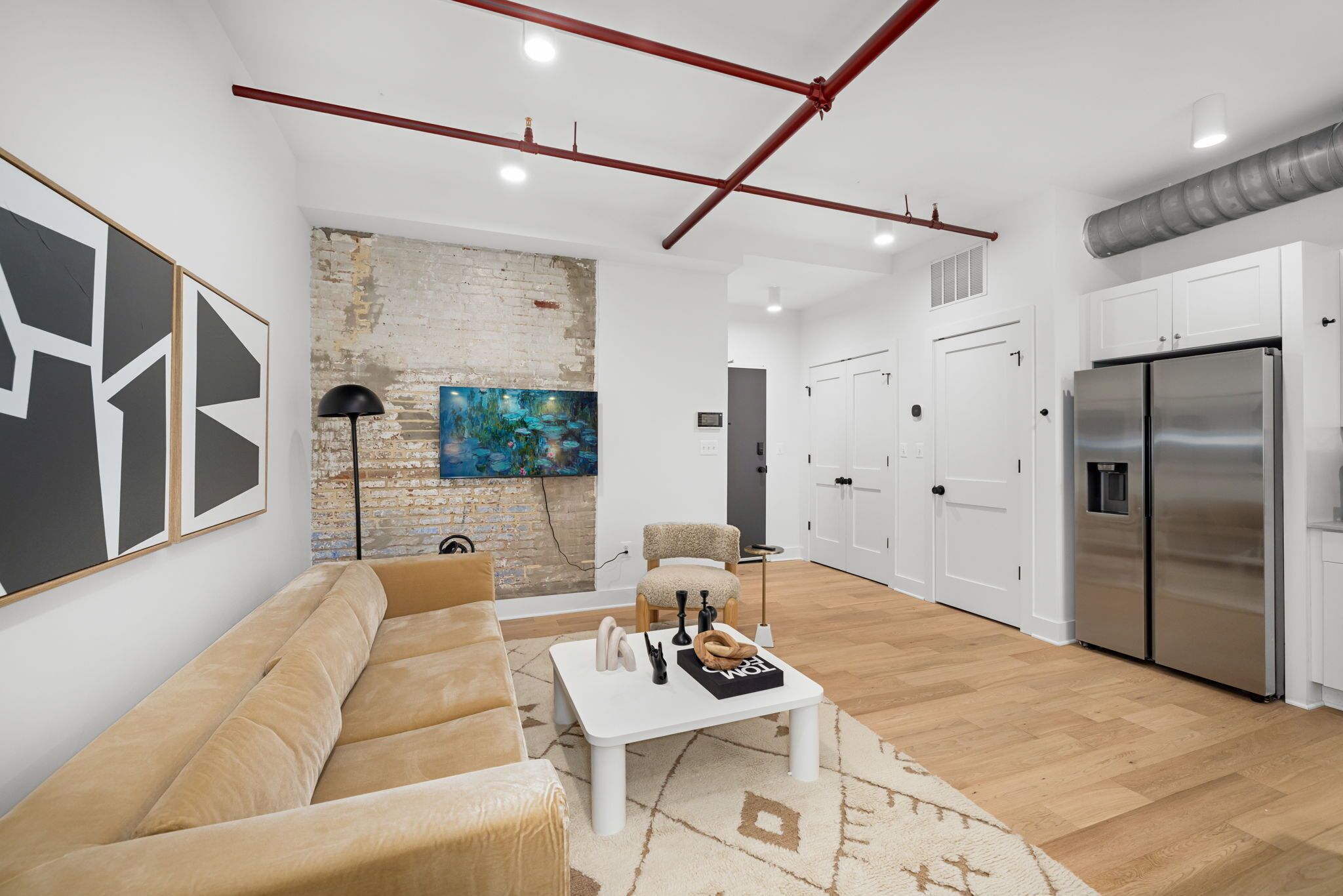 A modern living room with a beige sofa, a white coffee table, and a painting on the brick wall.