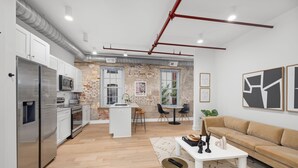 Una cocina moderna con electrodomésticos de acero inoxidable, una isla central y un comedor con pared de ladrillo de fondo.