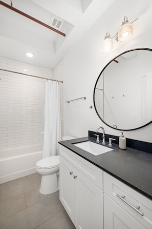 A modern bathroom with a bathtub, toilet, and vanity with a sink and mirror.