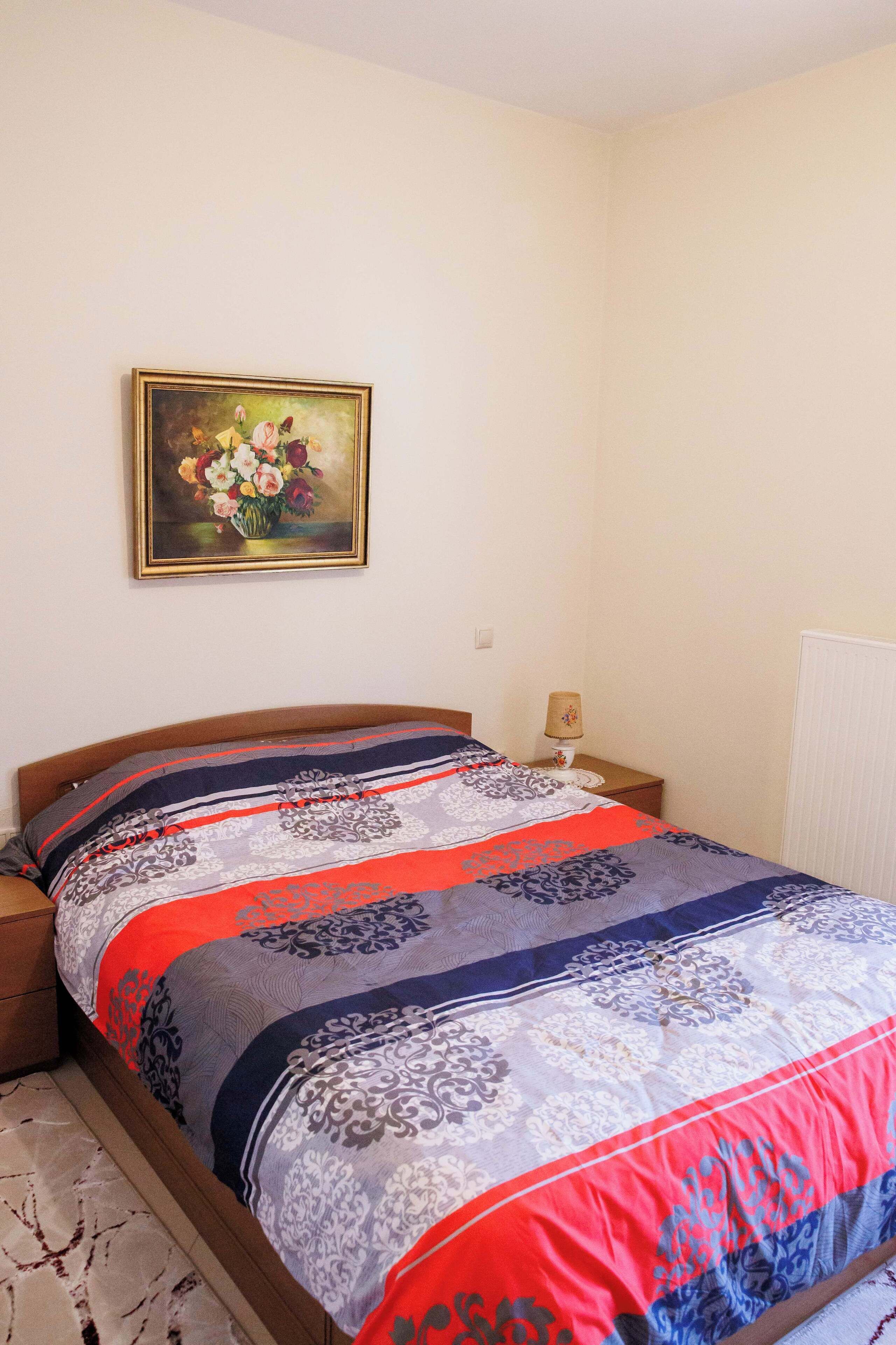 A bedroom with a bed, a nightstand, a lamp, and a painting on the wall.