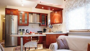 Una cocina moderna con armarios de madera, un refrigerador de acero inoxidable y un comedor con mesa y banco blancos.