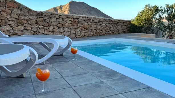 Un espace piscine avec des murs en pierre, des chaises longues et deux verres de boisson à l’orange.