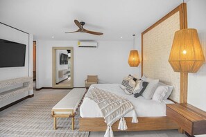 A modern bedroom with a bed, bedside tables, a bench, a ceiling fan, and a large wall-mounted TV. - Casa Que Chiva (Reserva de Golf, Hacienda Pinilla)