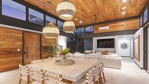 A modern interior with a large dining table, wicker chairs, and a central plant. - Casa Que Chiva (Reserva de Golf, Hacienda Pinilla)