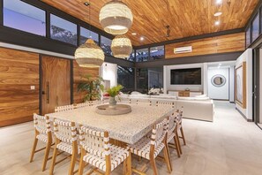 Ein modernes Interieur mit einem großen Esstisch, Korbstühlen und einer zentral platzierten Pflanze.