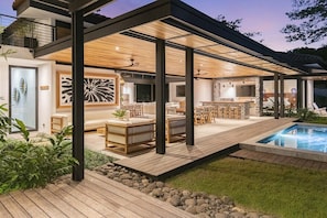A modern outdoor living space with a pool, wooden deck, and seating area. - Casa Que Chiva (Reserva de Golf, Hacienda Pinilla)