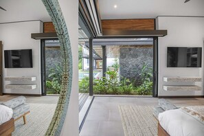 Ein modernes Schlafzimmer mit einem großen Schiebeglastür, die zu einem Garten führt, inklusive integriertem Fernseher und einer Wand mit Steinakzenten.