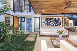 A modern outdoor living area with a white sofa, a dining table, and a ceiling fan.