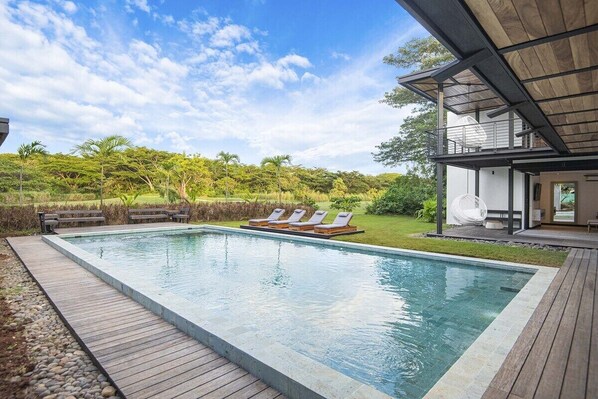 A swimming pool with lounge chairs and a deck, surrounded by greenery and a building with a modern design.