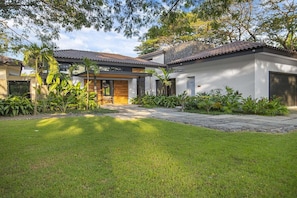 A modern house with a paved driveway, a wooden door, and a garage. - Casa Que Chiva (Reserva de Golf, Hacienda Pinilla)