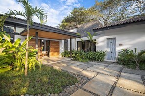 A modern house with a patio, stone pathway, and tropical plants. - Casa Que Chiva (Reserva de Golf, Hacienda Pinilla)