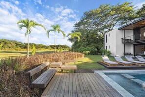 A pool area with wooden deck, lounge chairs, and a modern building with a balcony. - Casa Que Chiva (Reserva de Golf, Hacienda Pinilla)