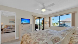 Un dormitorio con cama, televisión, ventilador de techo y vistas al exterior.