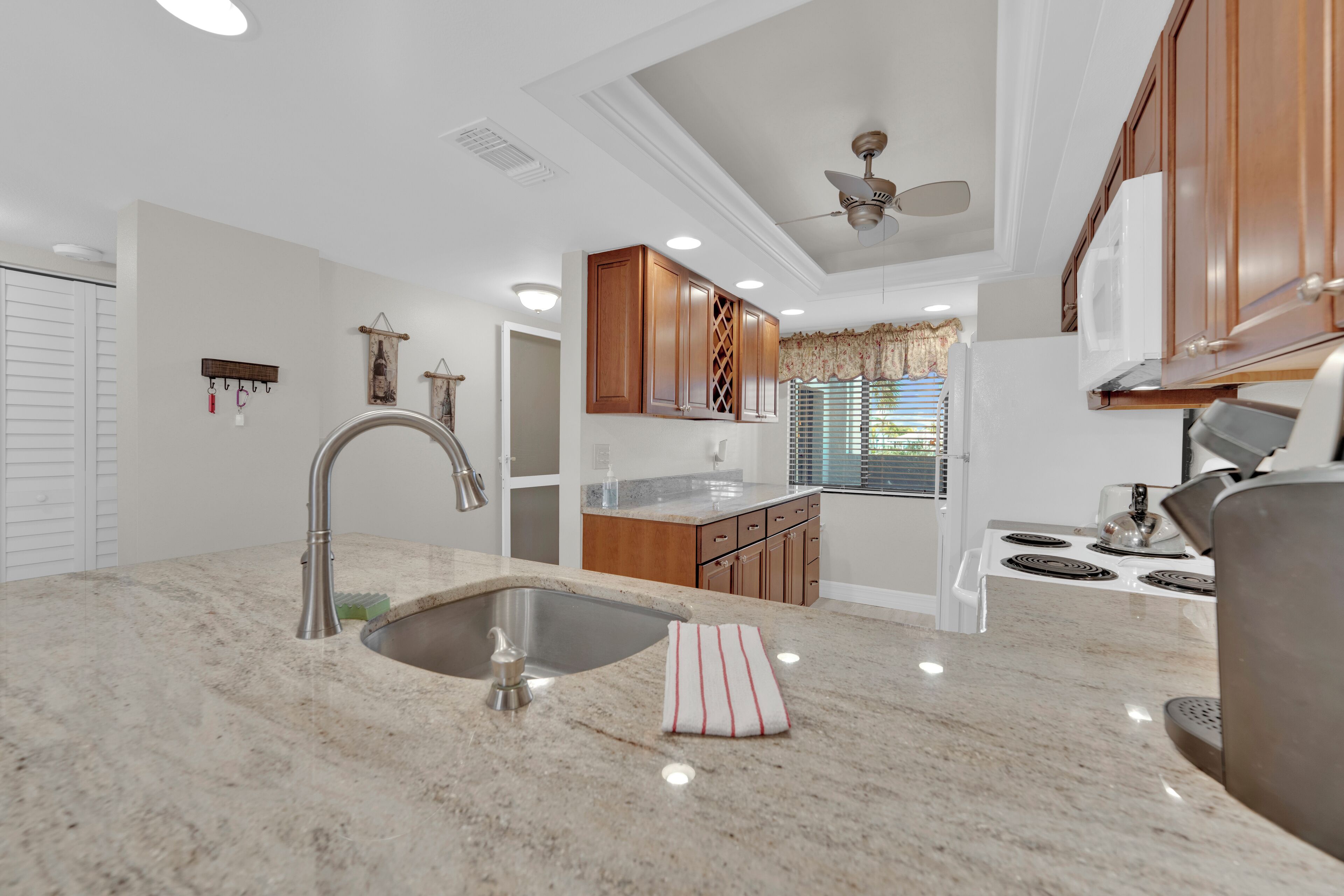 A modern kitchen with a granite countertop, stainless steel sink, wooden cabinets, and a ceiling fan.