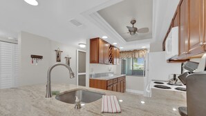 Una cocina moderna con encimera de granito, pileta de acero inoxidable, armarios de madera y ventilador de techo.
