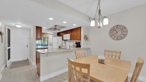 Una cocina moderna con armarios blancos, una mesa de comedor de madera y un reloj en la pared.