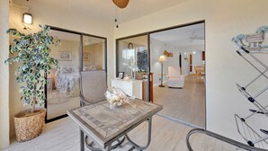 Una habitación con ventilador de techo, una mesa con adornos, una planta en maceta y un espejo grande que refleja otra habitación.
