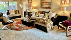 A modern living room with a sofa, armchairs, a coffee table, and a fireplace. There are paintings on the walls and a large window providing a view of the outdoors. - Luxury Wine Country Home With Pool Spa (Murrieta)