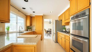 A modern kitchen with wooden cabinets, stainless steel appliances, a granite countertop, and a view to the dining area. - Luxury Wine Country Home With Pool Spa (Murrieta)