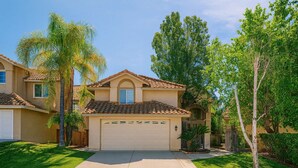A two-story house with a tiled roof, a garage, and a well-maintained lawn with palm trees. - Luxury Wine Country Home With Pool Spa (Murrieta)
