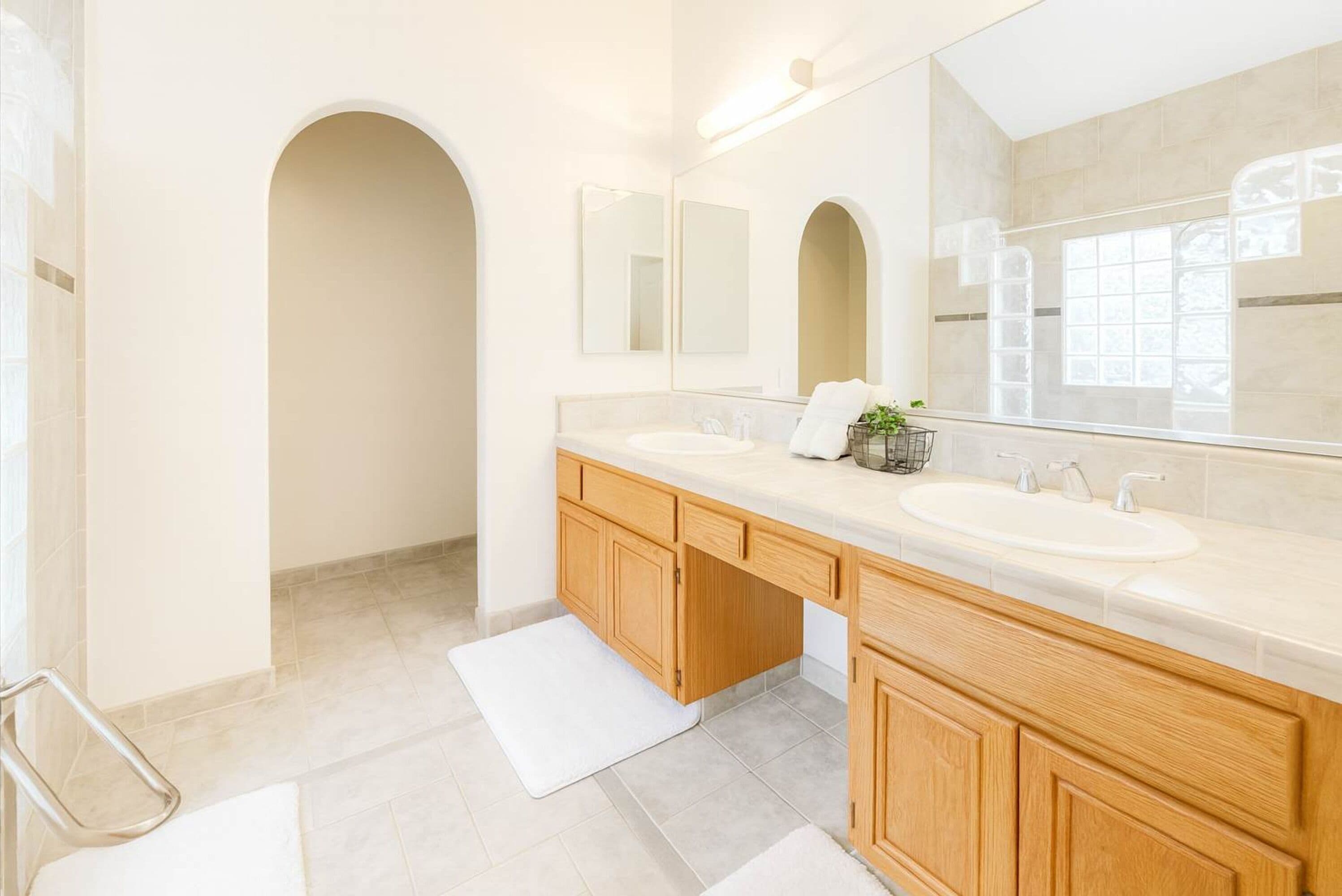 Un bagno moderno con due lavabi, mobili in legno, uno specchio grande e un pavimento piastrellato.