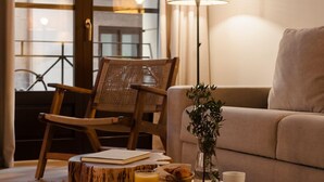 Ein gemütlicher Wohnbereich mit einem Holzstuhl, einer Couch, einem Tisch mit einem Buch, einem Glas Orangensaft und einer Lampe.