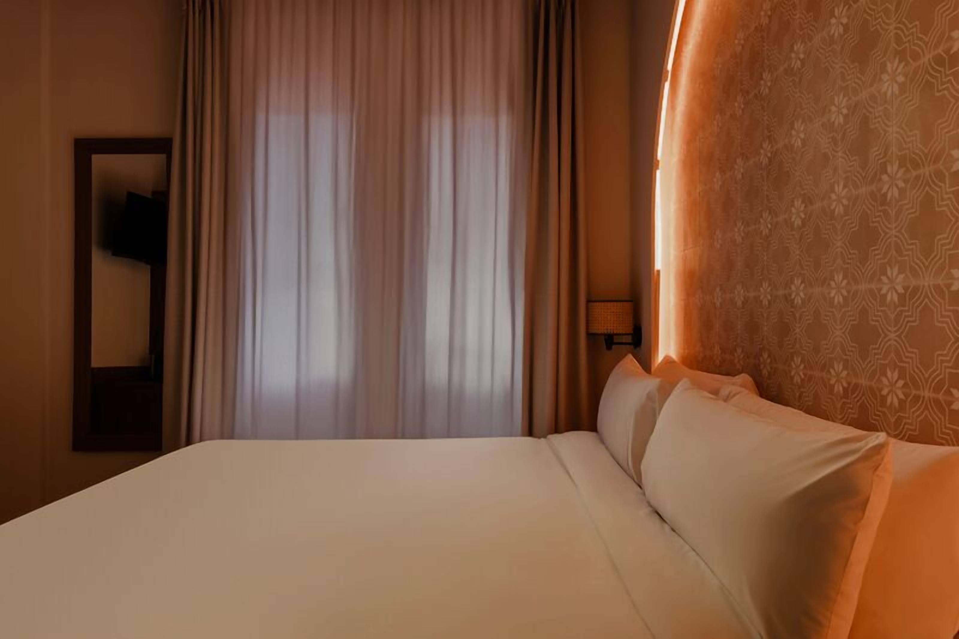 A hotel room with a large bed, a mirror, and a window with curtains.
