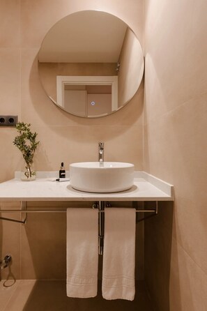 A bathroom with a round mirror, a white sink, a vase with green plants, and two towels hanging. - Hamsa House (Barcelona)