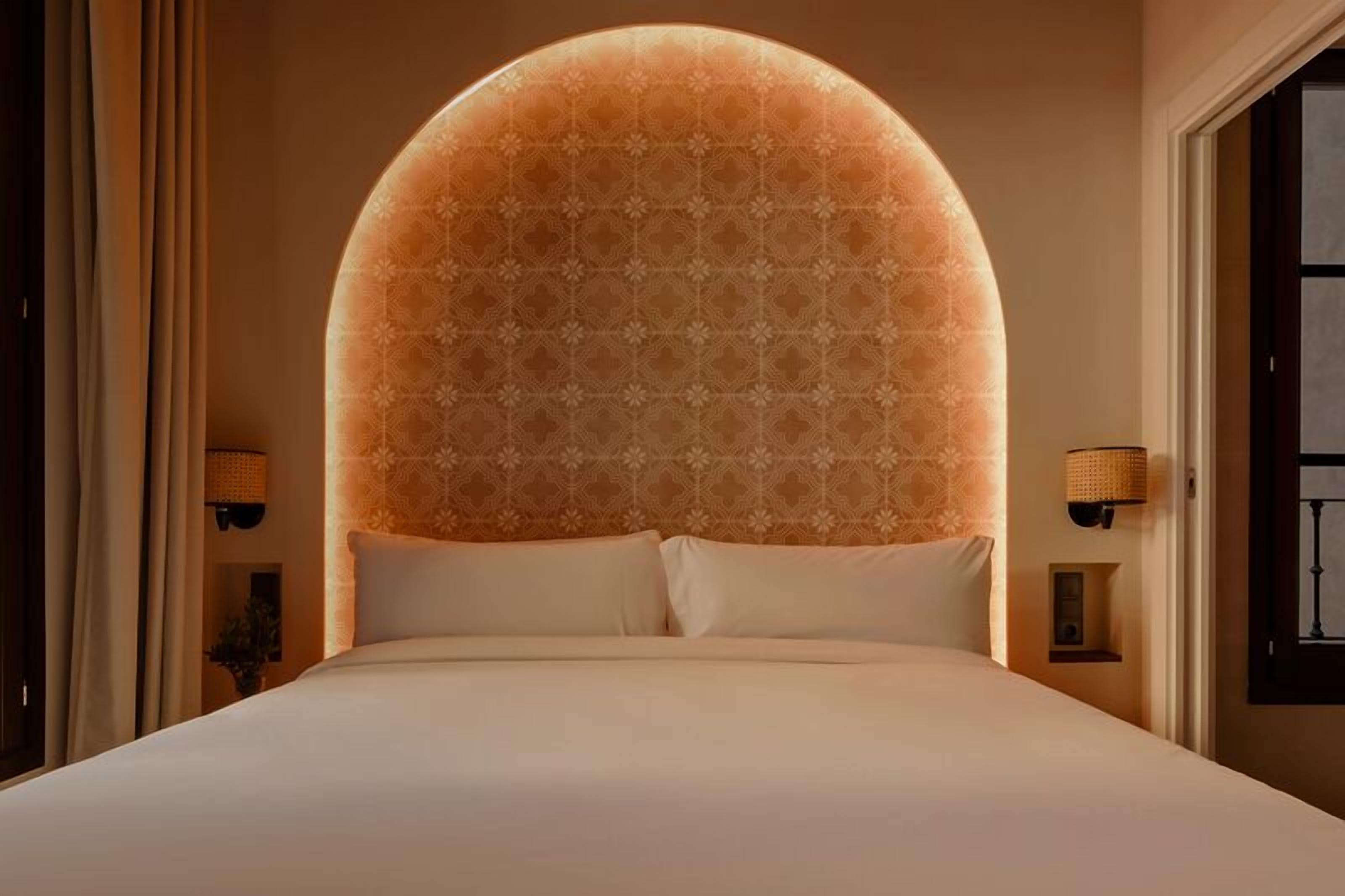 Un grand lit avec une tête de lit décorée, deux lampes de chevet et une vue sur une fenêtre.