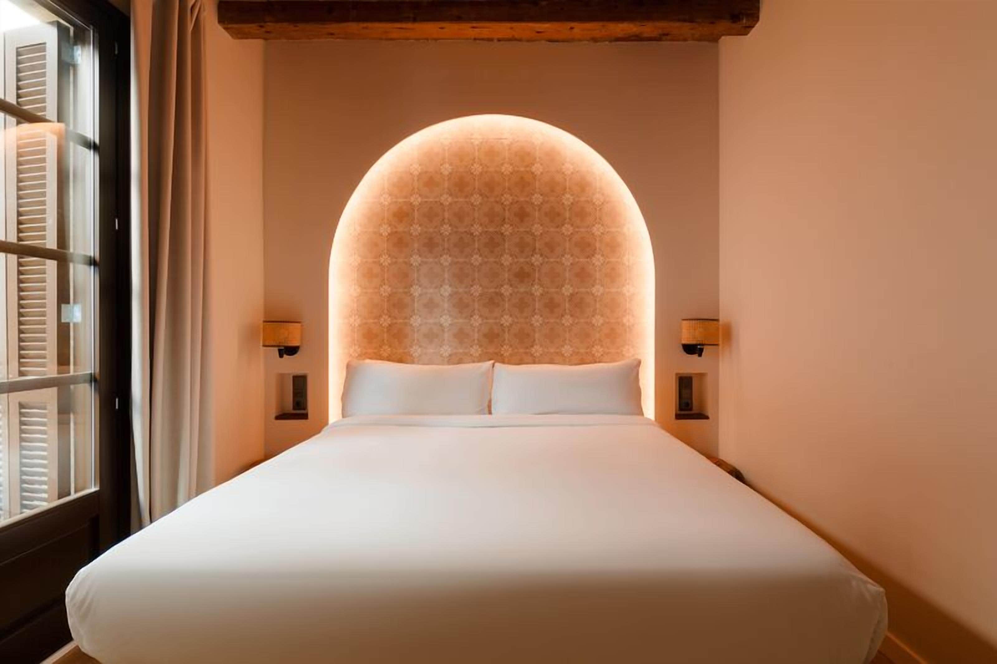 A neatly made bed with a large, illuminated dome-shaped ceiling light fixture above it.